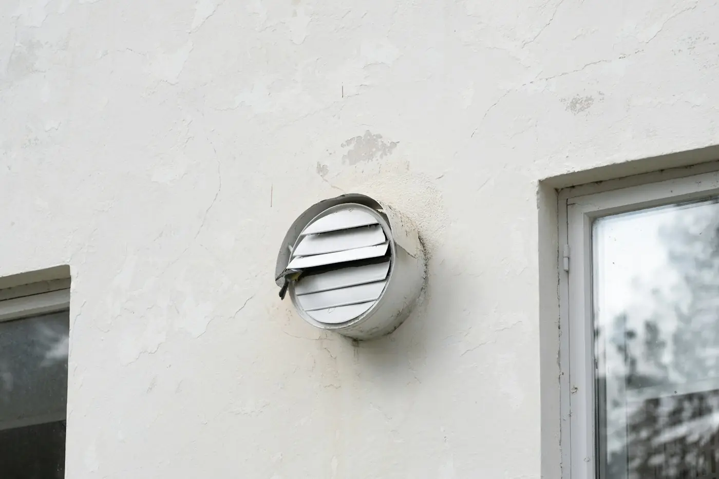 Round dryer vent hood on a white stucco wall